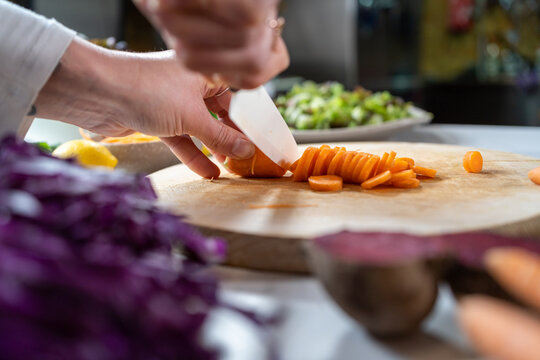 Crop unrecognizable female cutting raw carrot with knife while preparing vegetarian food in house