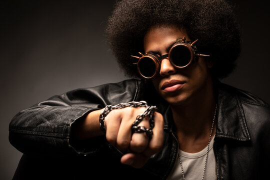 Trendy African American male in leather jacket and contemporary sunglasses with Afro hairstyle on gray background