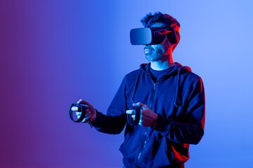 Anonymous unshaven male in hoodie and modern goggles with controllers and extended arm experiencing virtual reality