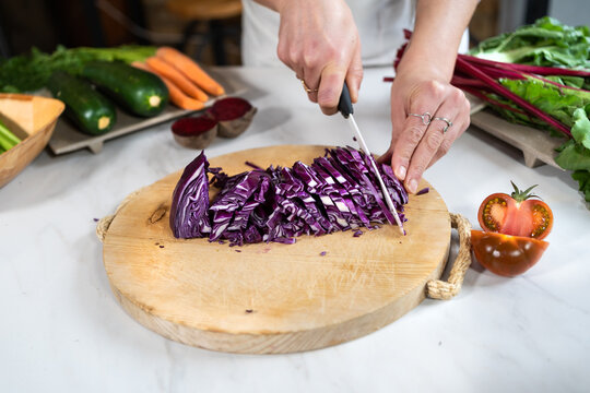 Cropped unrecognizable female cutting red cabbage with knife while preparing vegetarian food at table in loft style house