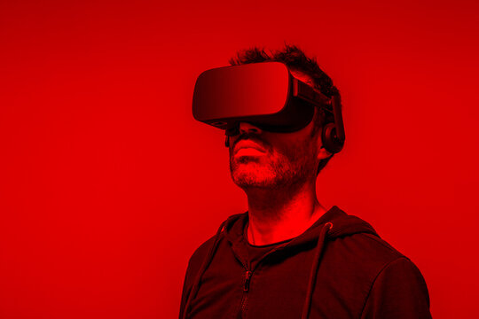 Unrecognizable bearded male in hoodie and modern headset exploring virtual reality in neon light