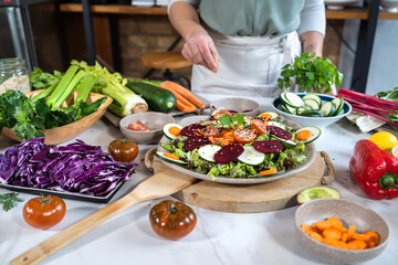 Crop anonymous female preparing delicious vegetable salad with sesame seeds at table in house kitchen