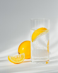 Glass of clean mineral sparkling water with ice and lemon on a white background with sunshine