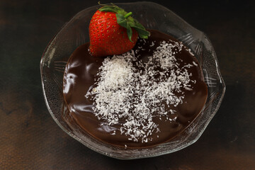 Chocolate pudding in a glass bowl, coconut and strawberries on it. Local name Supangle