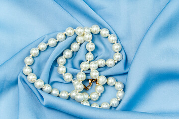 costume jewellery necklace made of white pearls on bright blue satin fabric