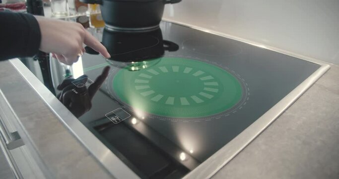 Woman activates futuristic hotplate stove with touch elements and sets temperature in modern kitchen
