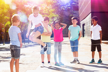 Obraz premium Smiling children playing rubber band jumping game and laughing outdoor