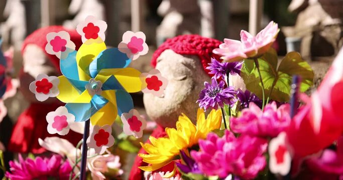 A slow motion of moving colorful windmills with Jizo statue daytime closeup