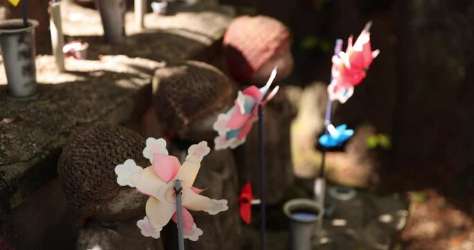 A slow motion of moving colorful windmills with Jizo statue daytime