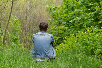 Obraz premium Young man sitting in spring forest, back view 