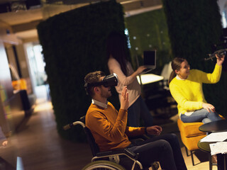 Disabled businessman in a wheelchair at work in modern open space coworking office with team using virtual reality googles drone assistance simulation