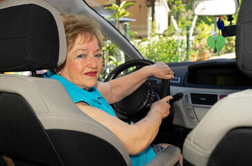 Beautiful lady in a blue shirt in her 70s is driving a car