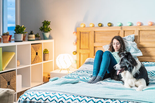 Young woman in glasses sitting on bed with border collie dog
