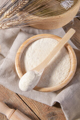 Whole wheat durum flour on a scooped wooden spoon and in wooden bowl with spikelets and sieve on a natural wooden background