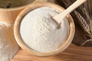 Whole wheat durum flour in wooden bowl with spoon on a natural wooden background, close up