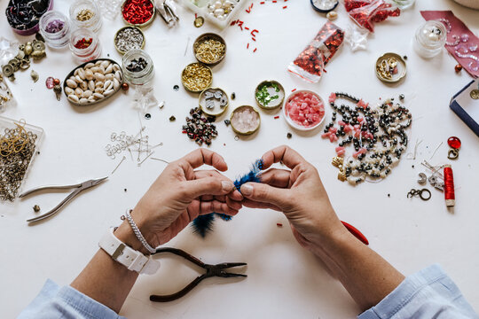 High angle of crop designer with pincers making decorative bijouterie sitting at table with different crystals and sequins
