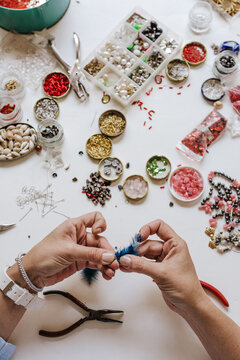 High angle of crop designer with pincers making decorative bijouterie sitting at table with different crystals and sequins