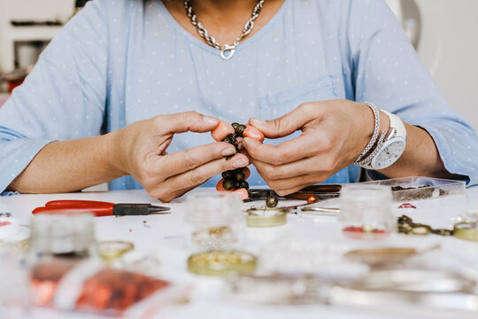Front view of crop anonymous female master with instrument making necklace at table with different tools