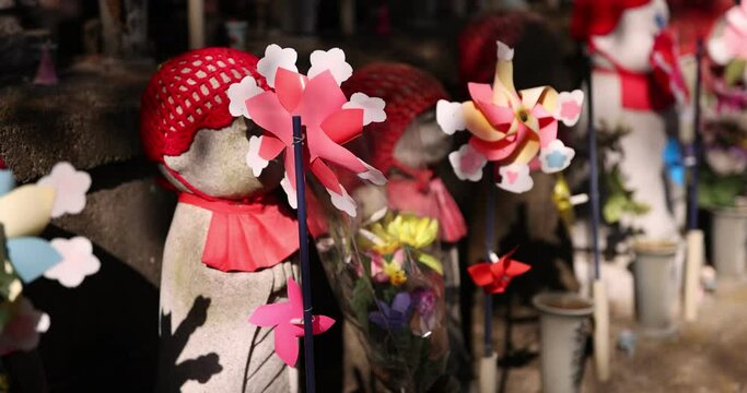 A slow motion of moving colorful windmills with Jizo statue daytime closeup