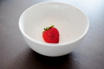 One ripe strawberry in white bowl on dark wooden background, high angle veiw