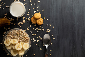 Desayuno saludable de avena con plátano, un vaso de leche y unas galletas sobre la mesa de color...
