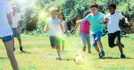 Obraz na płótnie Canvas Group of happy kids are running and playing football in park at summer day