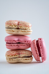 A stack of French macarons in pink and yellow with one macaron on the side, strawberry and vanilla macarons