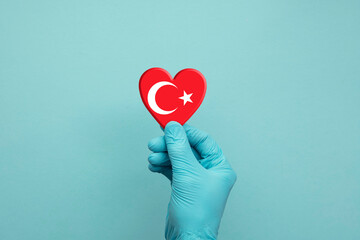 Hands wearing protective surgical gloves holding Turkey flag heart