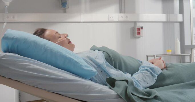 Side view of sick young woman with nasal cannula lying in hospital bed.