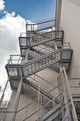 Fototapeta premium Metal fire escape stairs construction outdoor side of high building and blue sky with clouds. Pompier ladder.