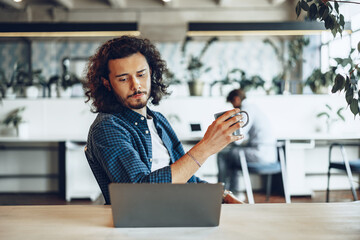 Young businessman is using laptop and holding a cup of coffee in office