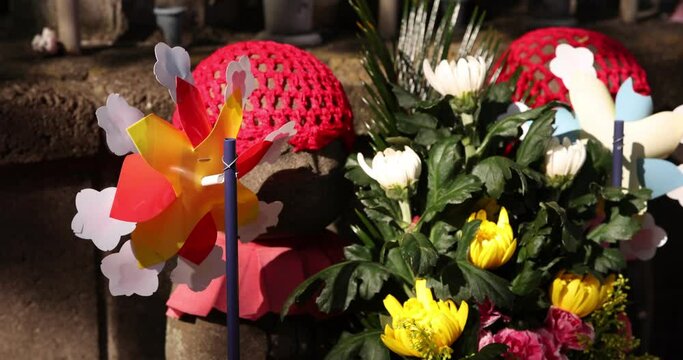 A slow motion of moving colorful windmills with Jizo statue daytime closeup