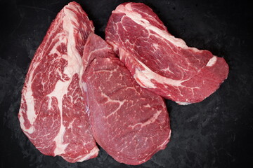 Raw Steaks. Sirloin Beef Steaks, Overhead View. Many Raw Striploin Steaks from Marbled Beef on Black Background. Group of Black Angus Beefsteaks. Raw Sirloin Cuts. Uncooked Prime Beef Steaks.