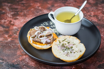 sandwich con chancho acompañado de una infusión de anis, en plato negro con fondo de textura marrón
