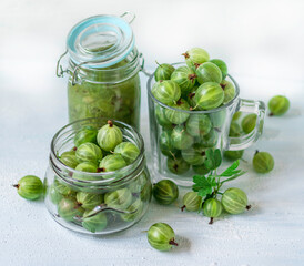 Gooseberry jam in a glass jar and berries scattered around. No-cook jam. Food background.