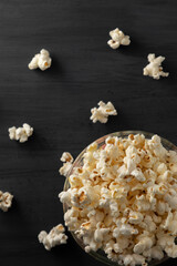 Palomitas de maíz en un recipiente con palomitas tiradas en la mesa de color negro