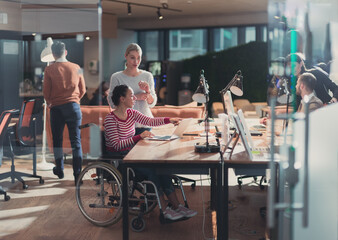 Disabled businesswoman in a wheelchair in modern coworking office space. Colleagues in background....