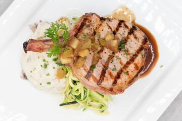 Overhead view of grilled pork chop served with mash potatoes and pasta to indulge that hearty appetite