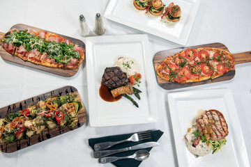 Overhead view of a table full of a flatbread choices, filet mignon, pork chop, brussel sprouts, or...