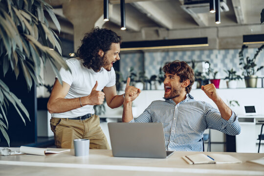 Two excited overjoyed young businessmen looking at laptop screen happy to win or recieved good news