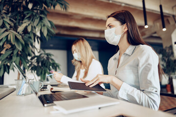 Two female colleagues working in office together wearing medical masks