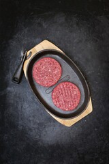 Raw Minced Homemade Grill Beef Burgers in Frying Pan, Top View. Griddle Grill Pap and Ground Beef Meat Patties for Grilling on Black Background, Overhead View. Raw Steak Burgers Cutlets On Grill Pan.