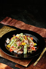 salad with ham, orange slices, tomato, cucumber and lettuce leaves in a black plate on a copper background. 