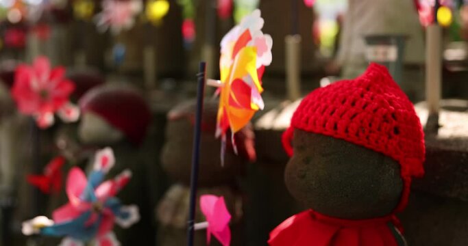 A slow motion of moving colorful windmills with Jizo statue daytime closeup