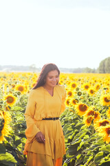 Fototapeta premium A brunette woman in a yellow dress on the field with sunflowers. Orange dress.