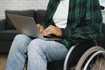 Disabled man sitting in a wheelchair and using laptop