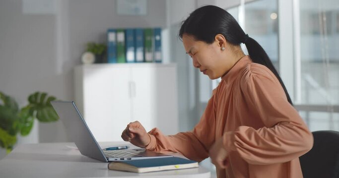 Asian businesswoman suffering from back pain at workplace.