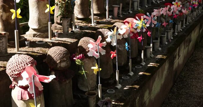A slow motion of moving colorful windmills with Jizo statue daytime