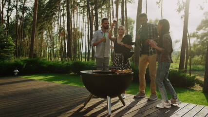 Happy people celebrating on grill party outside. Playful guys clinking glasses