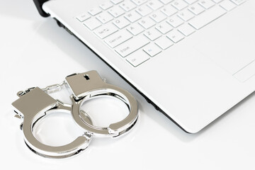 ノートパソコンと手錠。サイバー犯罪のイメージ